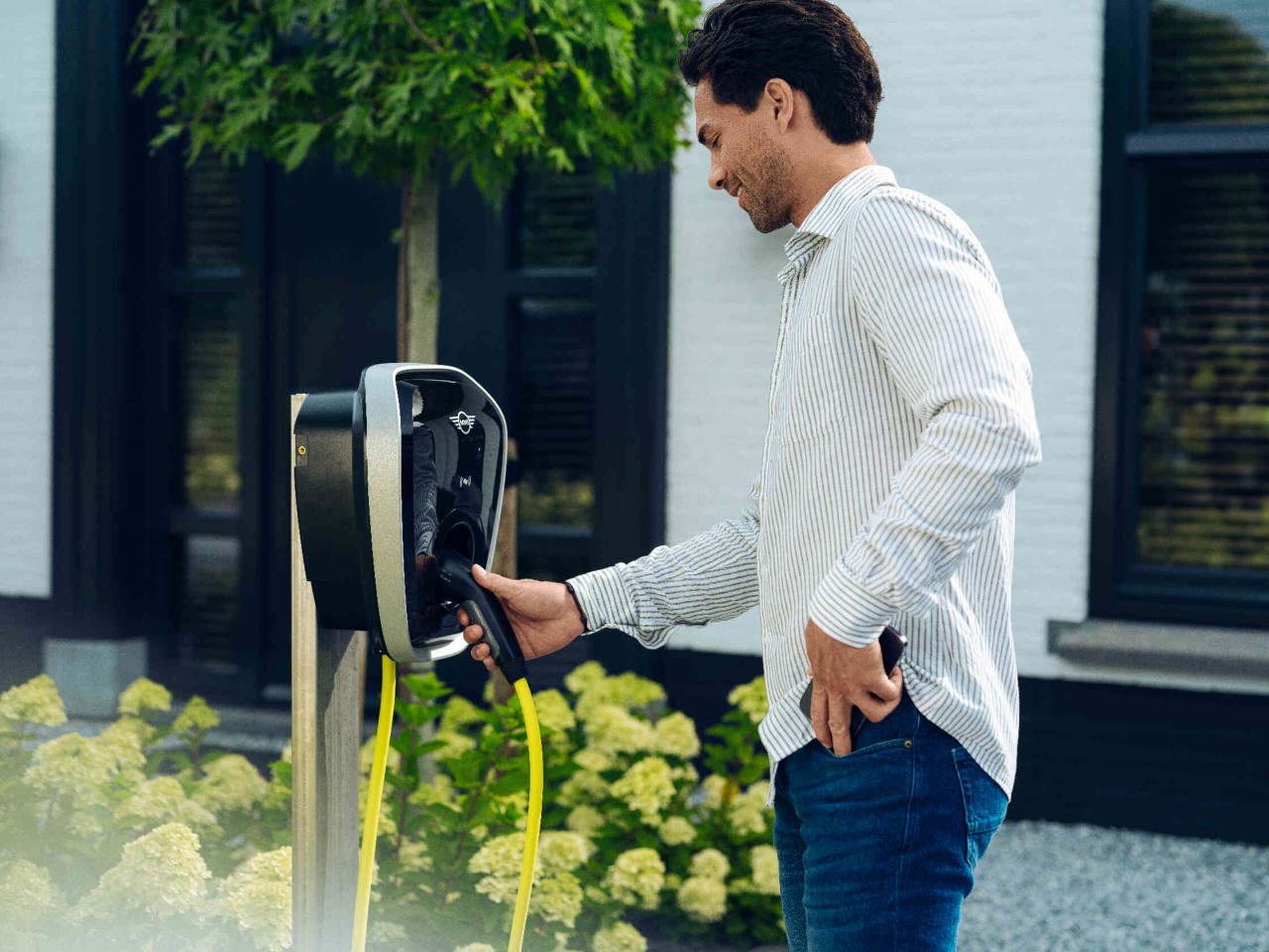 Man-laadstation-huis Man pakt de stekker van een E-laadstation en steekt zijn telefoon in zijn zak.