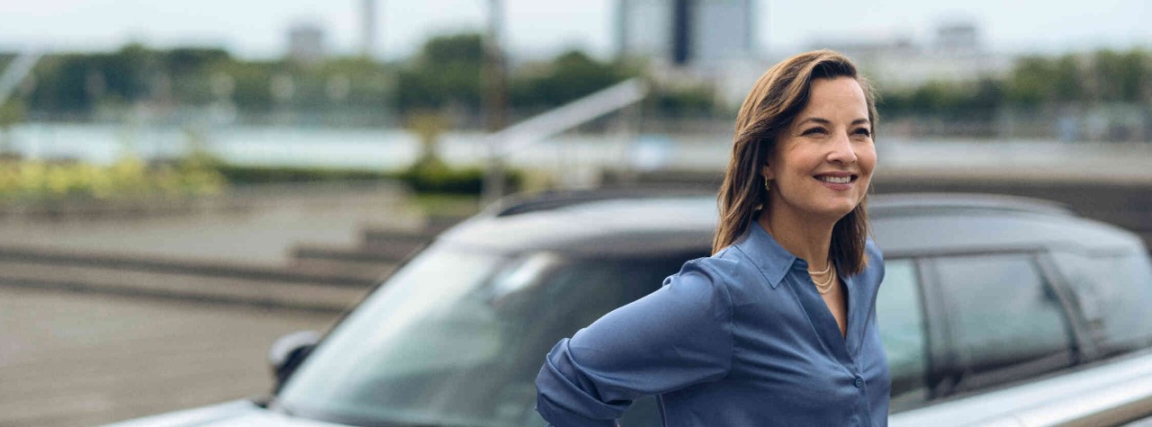 Frau MINI Fluss Frau lehnt an einem Gelaender Hintergrund zeigt ein weisses MINI Auto.